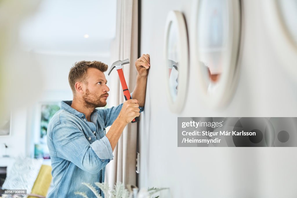 Handsome young man hammering nail on white wall