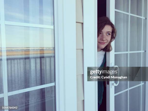 mischievous girl peeking out of a door at a beautiful view - peep window stock pictures, royalty-free photos & images