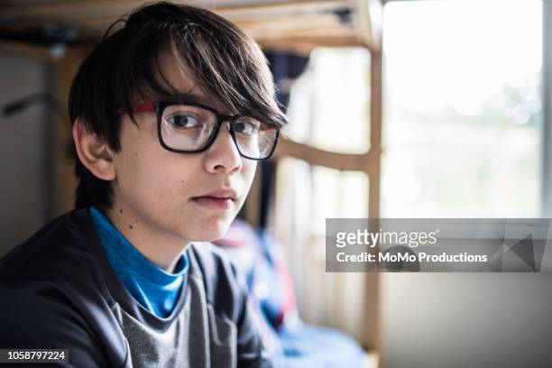 Portrait of young boy sitting on bed at home