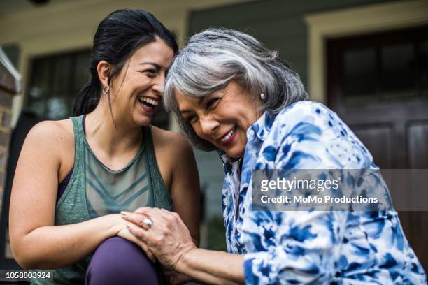 senior woman and adult daughter laughing on porch - lachen stockfoto's en -beelden