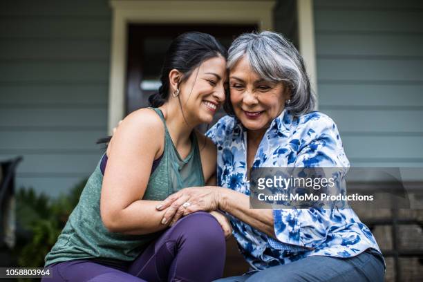 senior woman and adult daughter laughing on porch - erwachsene person stock-fotos und bilder