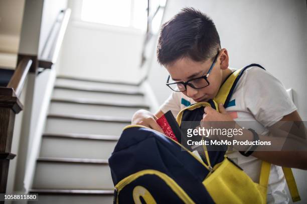school age boy looking through backpack - mochila bolsa fotografías e imágenes de stock