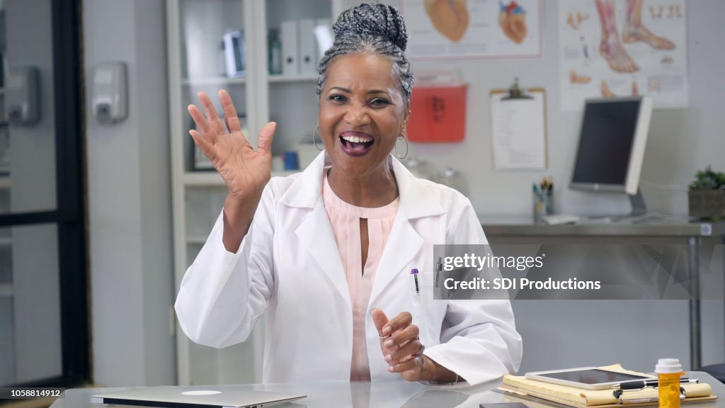 Female doctor waves at camera during web conference
