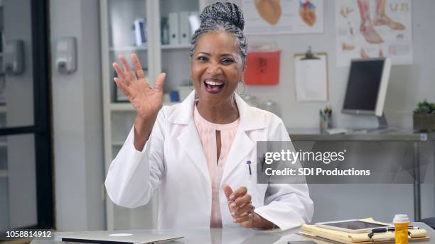 female doctor waves at camera during web conference - waving hi stock pictures, royalty-free photos & images