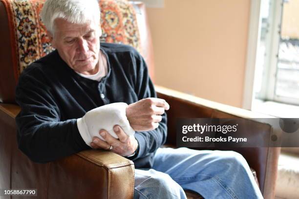 seated senior male with elastic compress on left wrist - compresse stock-fotos und bilder