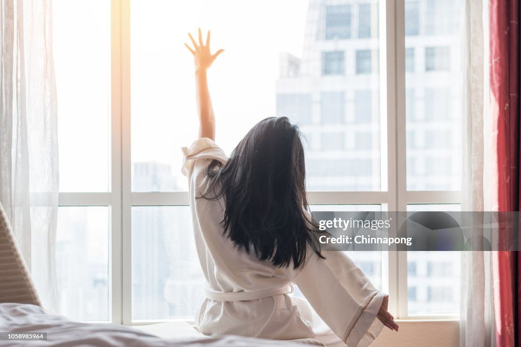 快樂的工作-生活品質平衡概念與簡單的生活方式亞洲女孩在床上有一個良好的一天醒來從良好的睡眠在週末早上休息, 懶洋洋地放鬆在舒適的臥室在城市酒店