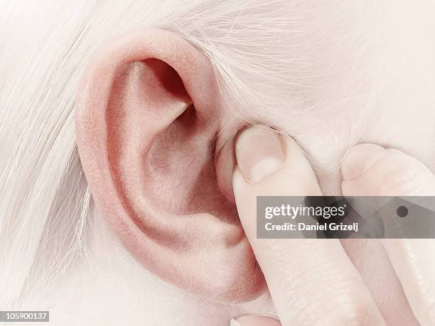 girl holding a finger over her ear - vingers in de oren stockfoto's en -beelden