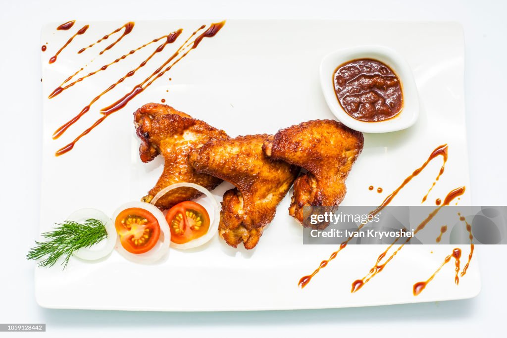 Honey chicken wings with onion, tomatoes, green and bbq sauce on white plate