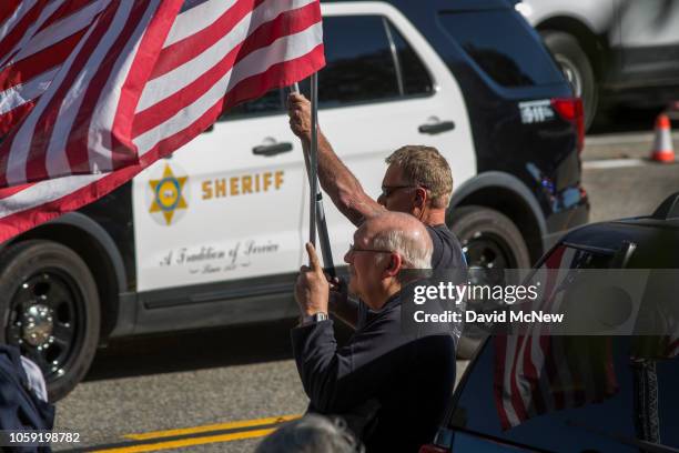 People hold flags as the procession carrying the body of Ventura County Sheriffs Sgt. Ron Helus, who was killed in a mass shooting at the Borderline...