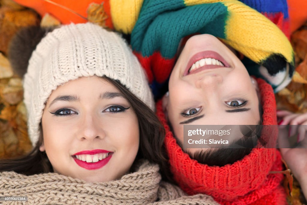 Two girlfriends lying on the dry autumn leaves