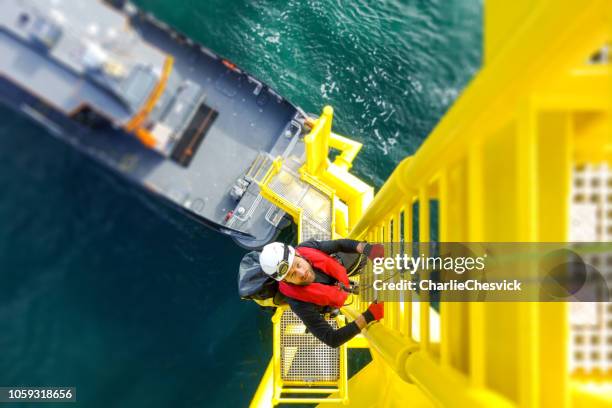 hoge arbeider offshore klimmen op wind turbine op de ladder - platform stockfoto's en -beelden