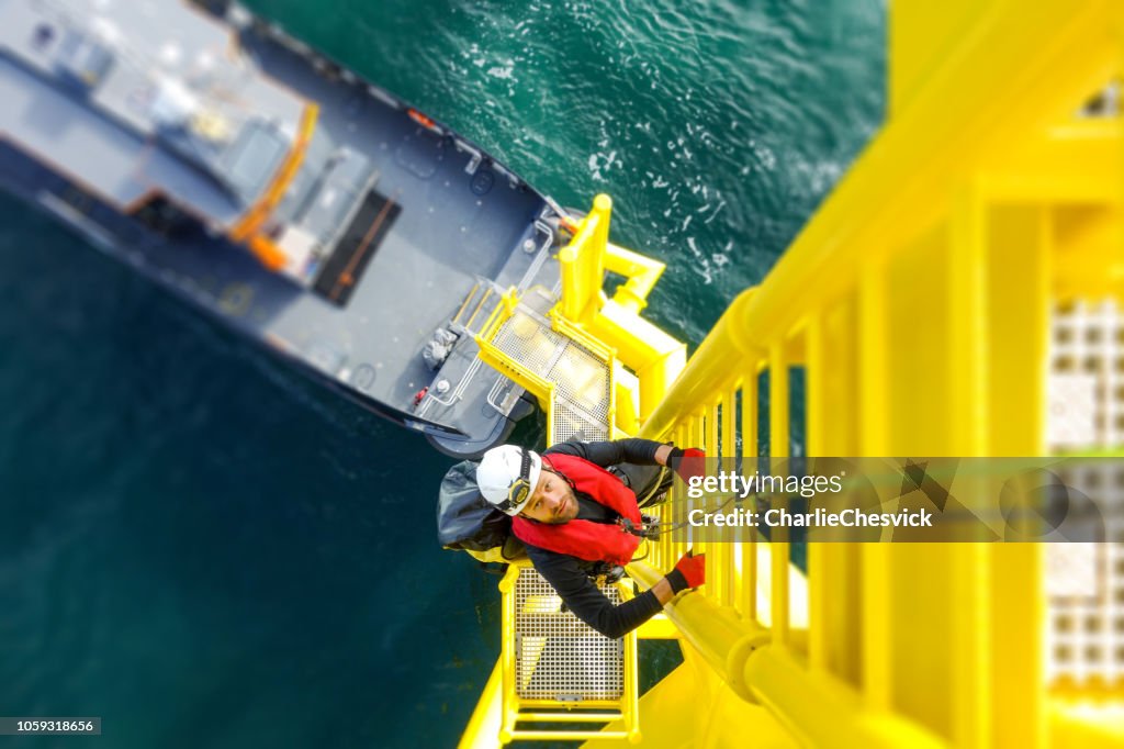 Manual high worker offshore climbing on wind-turbine on ladder