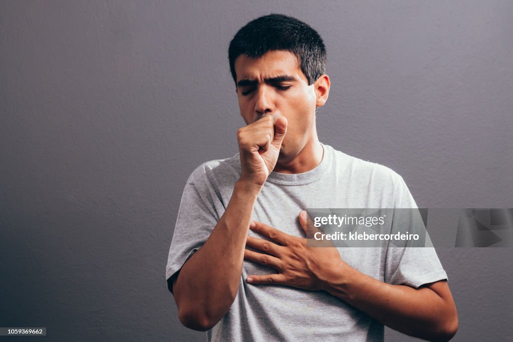 Man coughing into his fist, isolated on a gray background