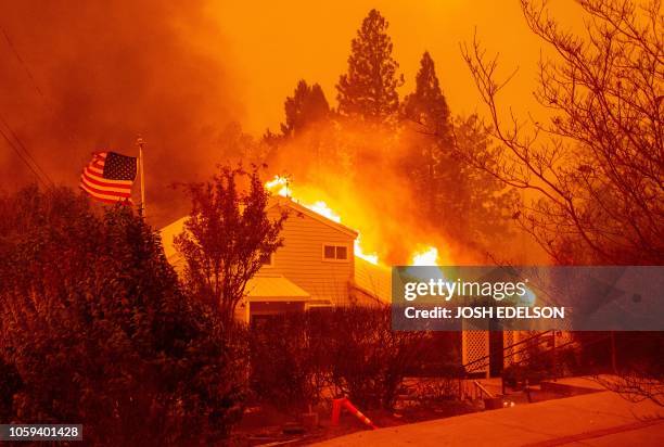An American flag waves in the wind as a home burns during the Camp fire in Paradise, California on November 8, 2018. - More than 18,000 acres have...