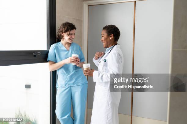 fröhliche krankenschwester und afroamerikaner arzt nehmen eine pause trinken kaffee und spaß im gespräch - hot nurse stock-fotos und bilder
