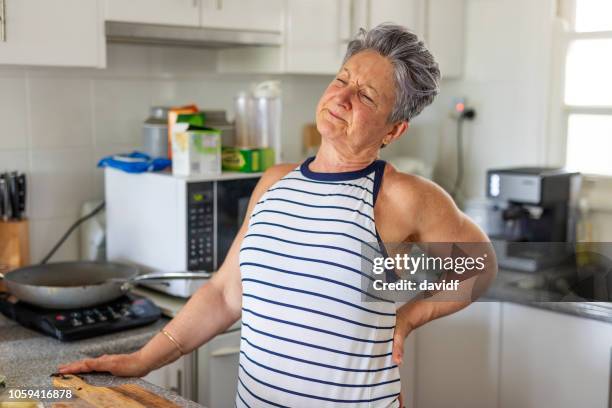 femme senior avec des maux de dos dans la cuisine - sciatique maladie photos et images de collection