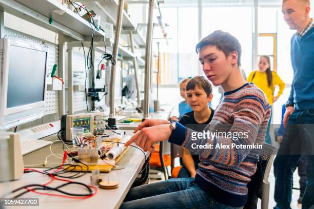 the group of kids of different ages, boys, and girls, working in the engineering laboratory - science exhibition stock pictures, royalty-free photos & images