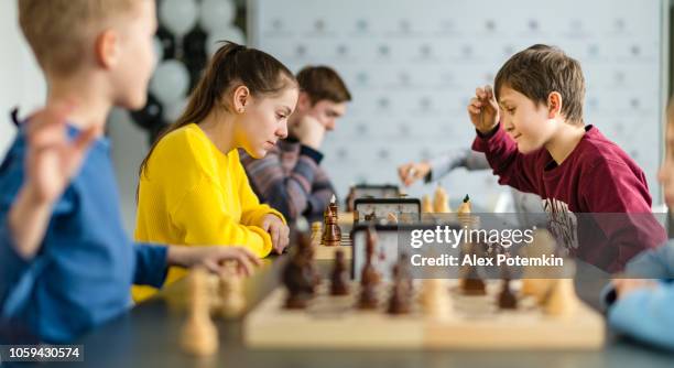 kids of different ages, boys and girls, playing chess on the tournament in the chess club - chess stock pictures, royalty-free photos & images