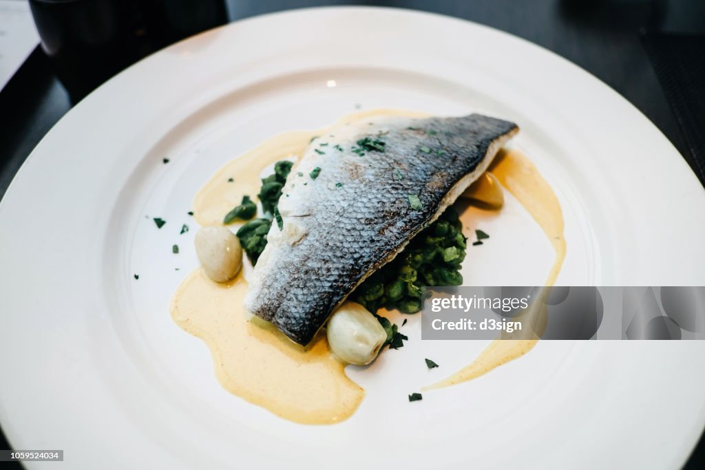 Delicate pan roasted fillet of white fish with vegetable and cream sauce freshly served on table in restaurant