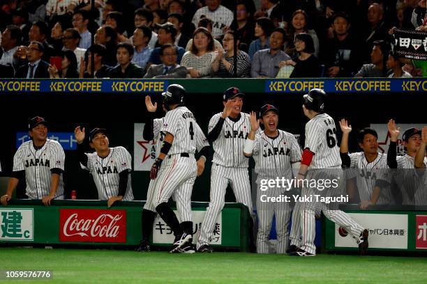 Ryosuke Kikuchi and Takuya Kai of Team Japan is greeted by teammates in the dugout after they both scored a run in the fifth inning during Game 1 of...