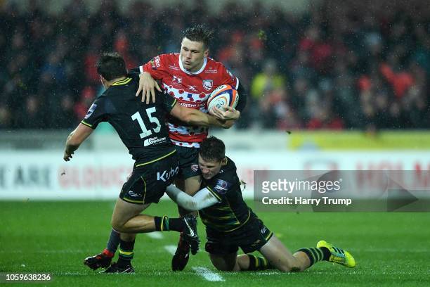 Jason Woodward of Gloucester is tackled by George Furbank and Fraser Dingwall of Northampton Saints during the Premiership Rugby Cup match between...