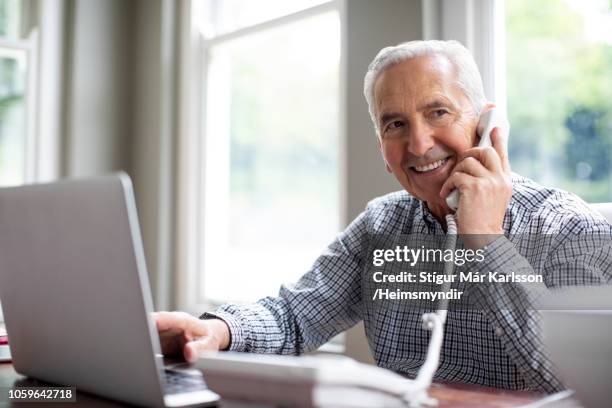 smiling man talking on phone while using laptop - telefone fixo imagens e fotografias de stock