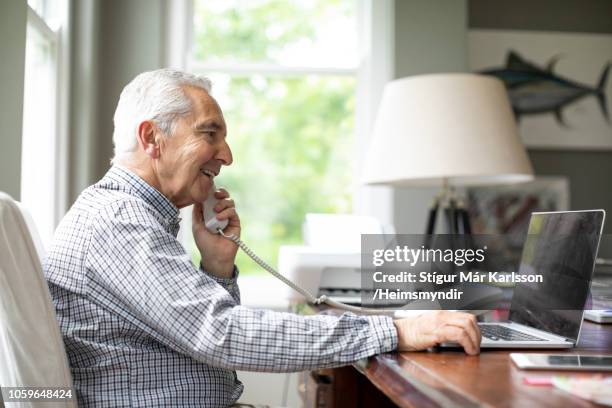 hombre sonriente, hablando por teléfono durante el uso del ordenador portátil - teléfono con cable fotografías e imágenes de stock