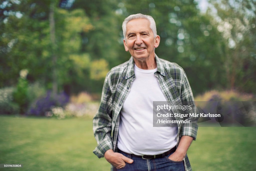 Retired man with hands in pockets at back yard