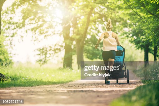 Running woman with baby stroller enjoying summer in park Running woman with baby stroller enjoying summer in park