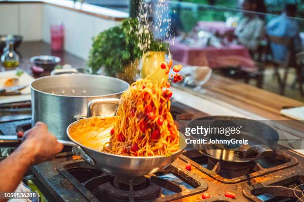 action shot of chef tossing fresh pasta in wok on gas hob - throwing tomatoes stock pictures, royalty-free photos & images