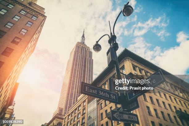 street sign of fifth ave and east 36th st with empire state tower in background at sunset in new york city. urban concept and road direction in manhattan downtown. - empire state building stock pictures, royalty-free photos & images