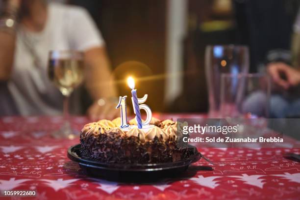 close-up of a chocolate and cream birthday cake with lighted candles and people gathered around it - 15th birthday stock pictures, royalty-free photos & images