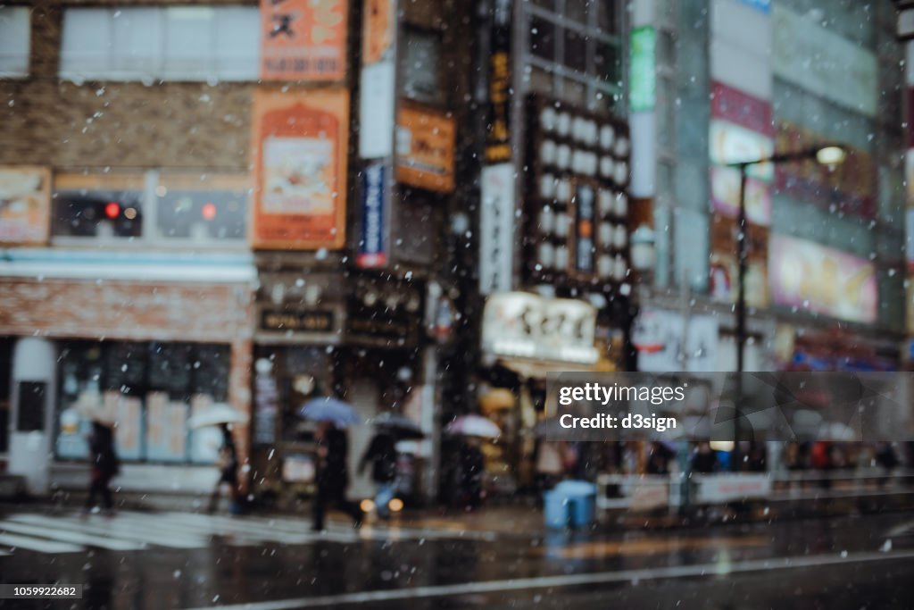 Blurred motion of pedestrians with umbrella walking in downtown city street in the snow