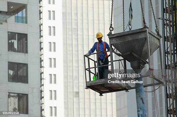Foreign worker helps guide a concrete funnel hoisted by a crane at a construction site among new highrise office buildings and hotels under...