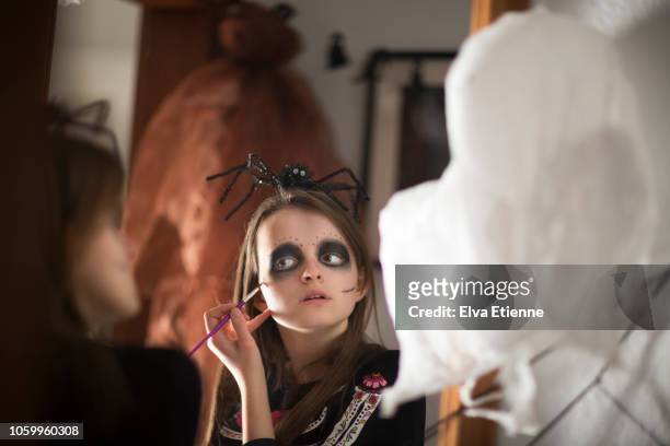 reflection in a mirror of a teenage girl applying halloween face paints to herself - kinder schminken stockfoto's en -beelden