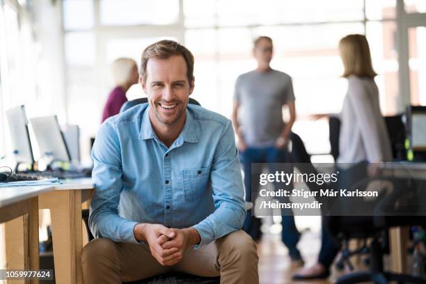 portrait of smiling businessman sitting at office - smart casual stock pictures, royalty-free photos & images