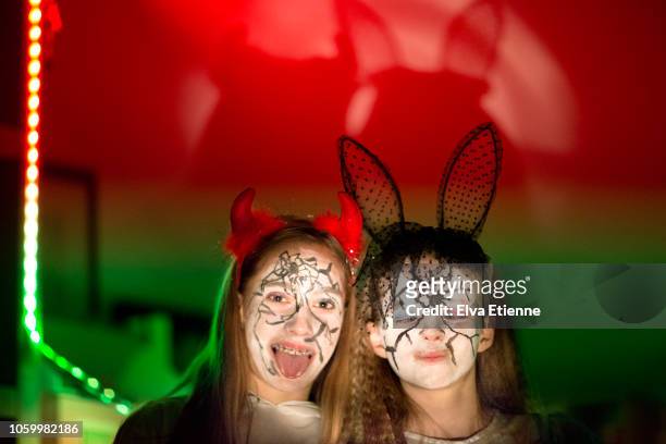 two girls pulling faces in halloween costumes, lit by torchlight with colourful background - serre tête photos et images de collection