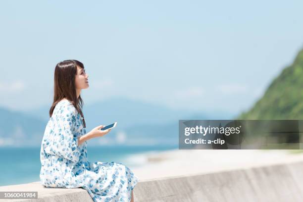 a woman who has a smartphone sitting on a breakwater - one embankment stock-fotos und bilder