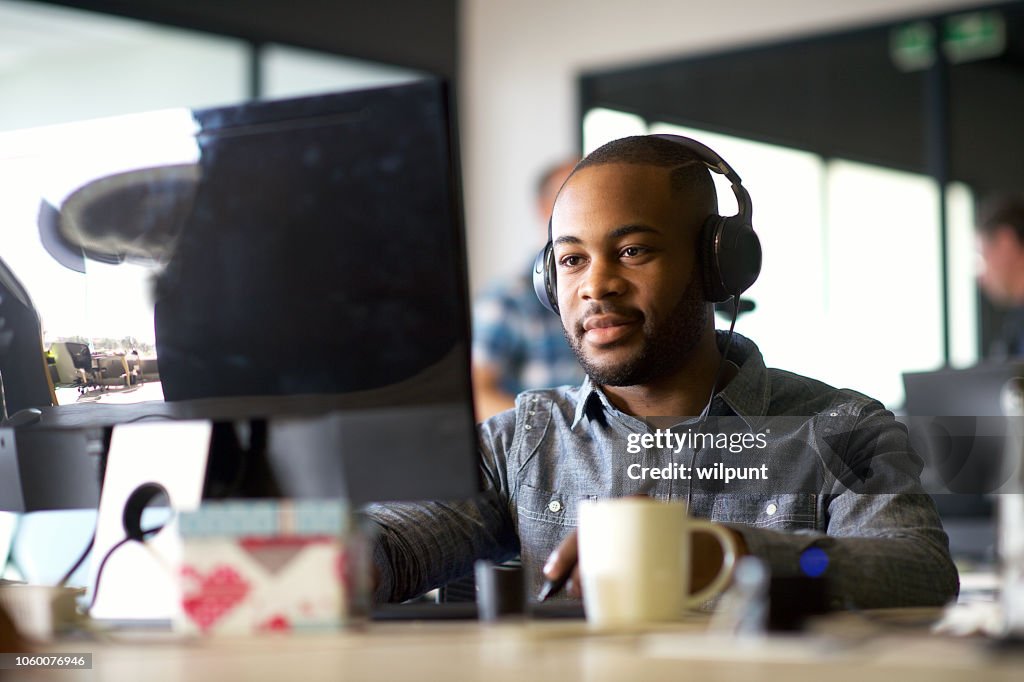 Young African Man with headphones looking at a computer monitor