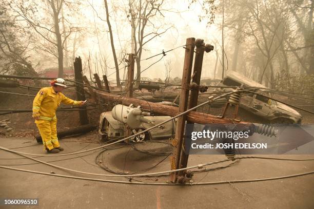 CalFire firefighter Scott Wit surveys burnt out vehicles near a fallen power line on the side of the road after the Camp fire tore through the area...