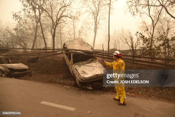 CalFire firefighter Scott Wit surveys burnt out vehicles on the side of the road after the Camp fire tore through the area in Paradise, California on...