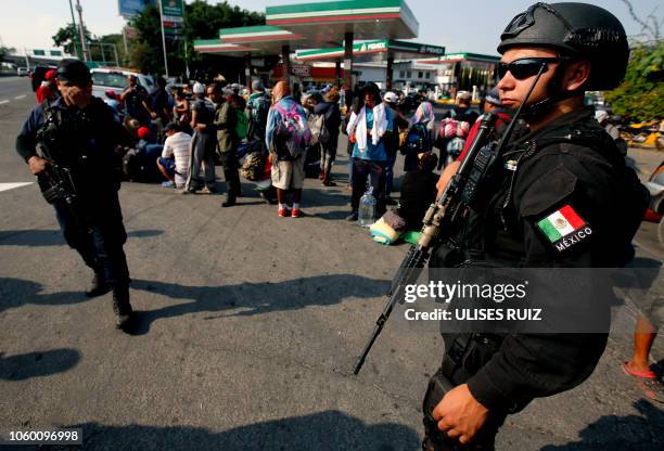 Police officers stand guard as Central American migrants moving in a caravan towards the United States in hopes of a better life or to escape...