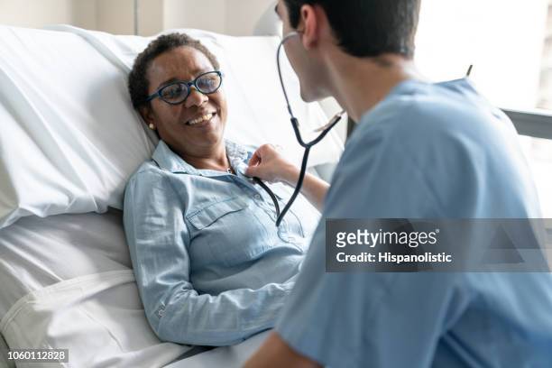 kvinnliga svart patienten liggande på sjukhussäng medan sjuksköterska kontrollerar hennes hjärta slå med stetoskop - black woman nurse bildbanksfoton och bilder
