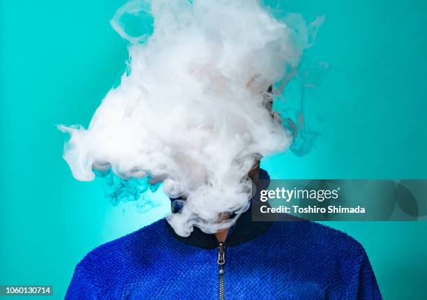 a masked man smoking vape and exhaling - fumée photos et images de collection