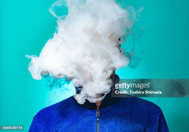 a masked man smoking vape and exhaling - electronic cigarette ストックフォトと画像