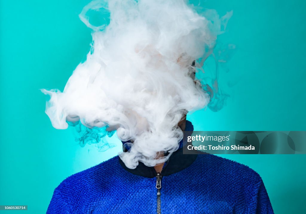 A masked man smoking vape and exhaling