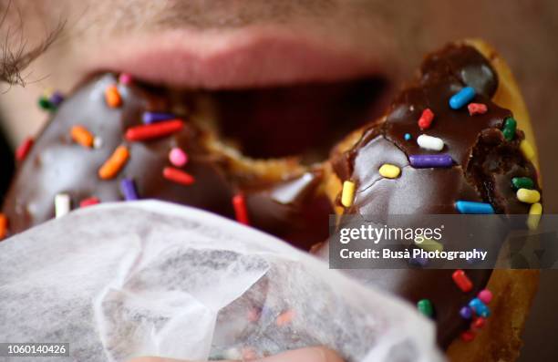 closeup of a mouth biting on chocolate glazed donut with sprinkles - chewed stock pictures, royalty-free photos & images