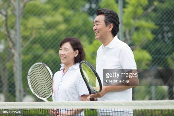 mature couple standing on a tennis court - japanese tennis stock-fotos und bilder
