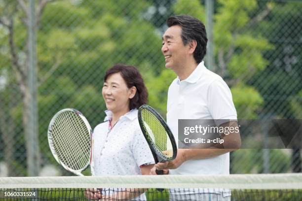 mature couple standing on a tennis court - japanese tennis photos et images de collection