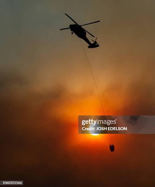 Helicopter passes by the sun as it makes a water drop in the Feather River Canyon, east of Paradise, California on November 11, 2018. - Search teams...